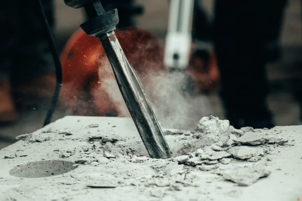Power tool chipping out damaged concrete before an SREM repair patch in a Local Law 126 garage
